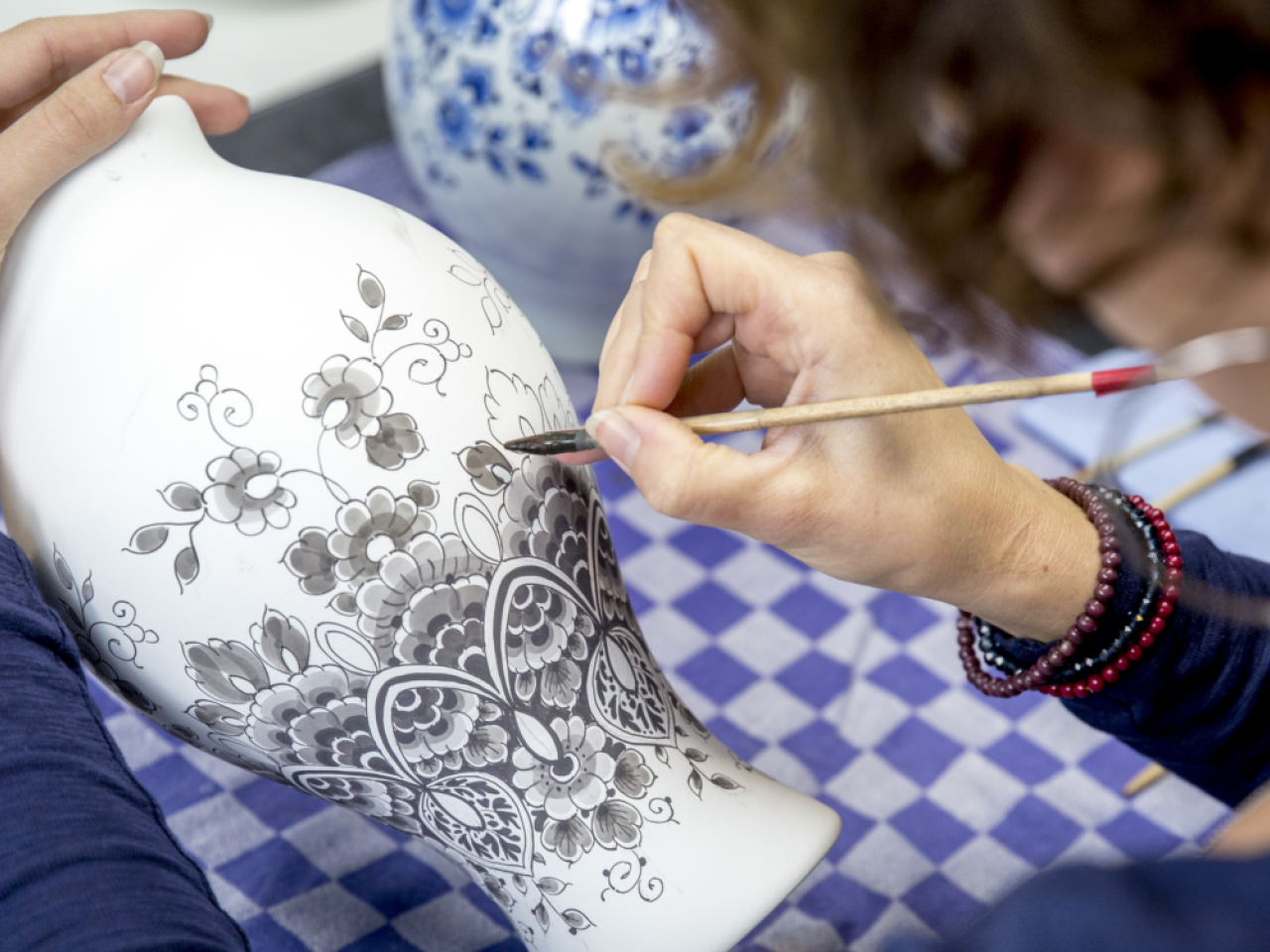 Delfts blauw schilder aan het werk bezig met het beschilderen van een vaas Heinen Delfts Blauw