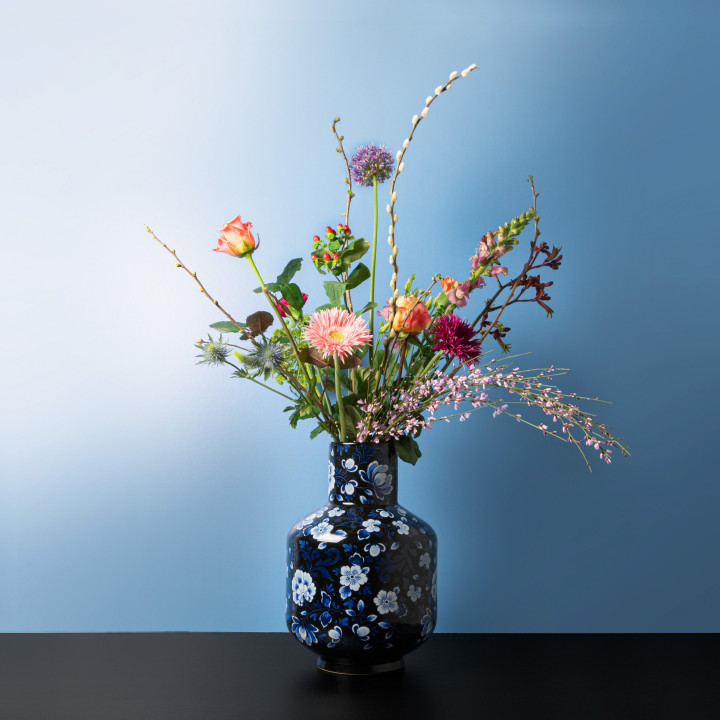 Hoge bolvaas zwart met Delfts blauwe versieringen en een klerrijke bos bloemen.